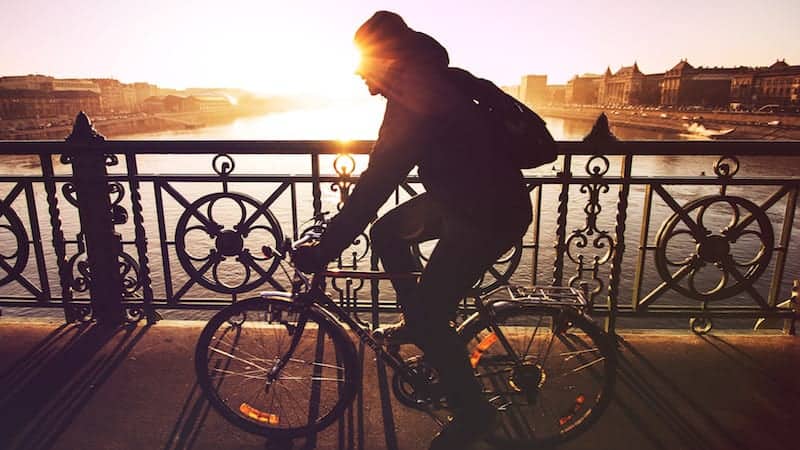 man riding a bike across bridge at sunset
