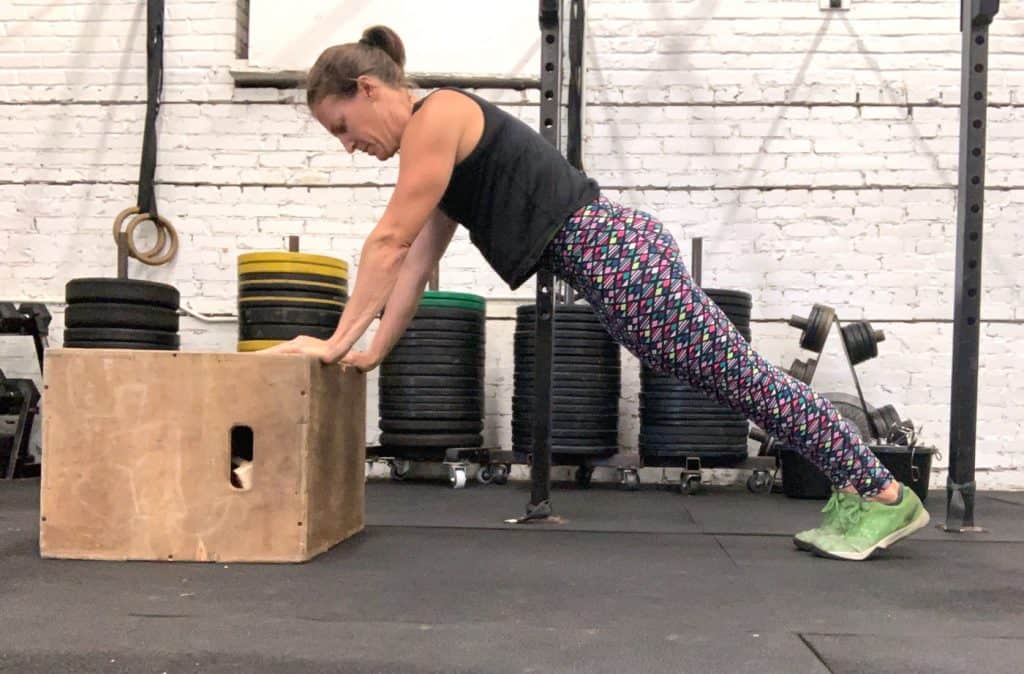 woman in a gym doing a push up with hands elevated on a box