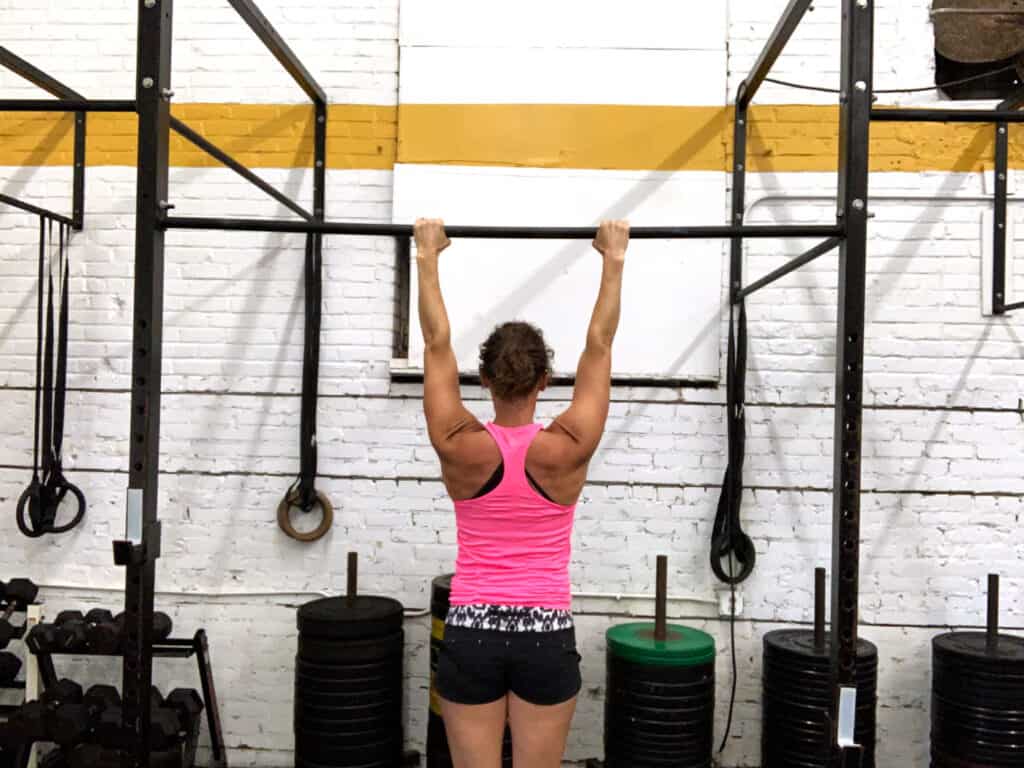 back view of woman hanging from pull up bar with an active shoulder