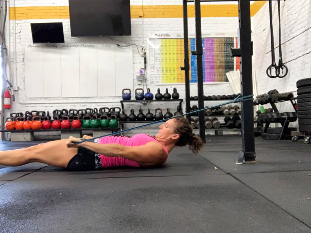 woman lying on floor of gym doing banded lat pull downs